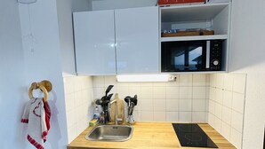 Cocina compacta con armarios blancos, encimera de madera, pileta, microondas y heladera pequeña.