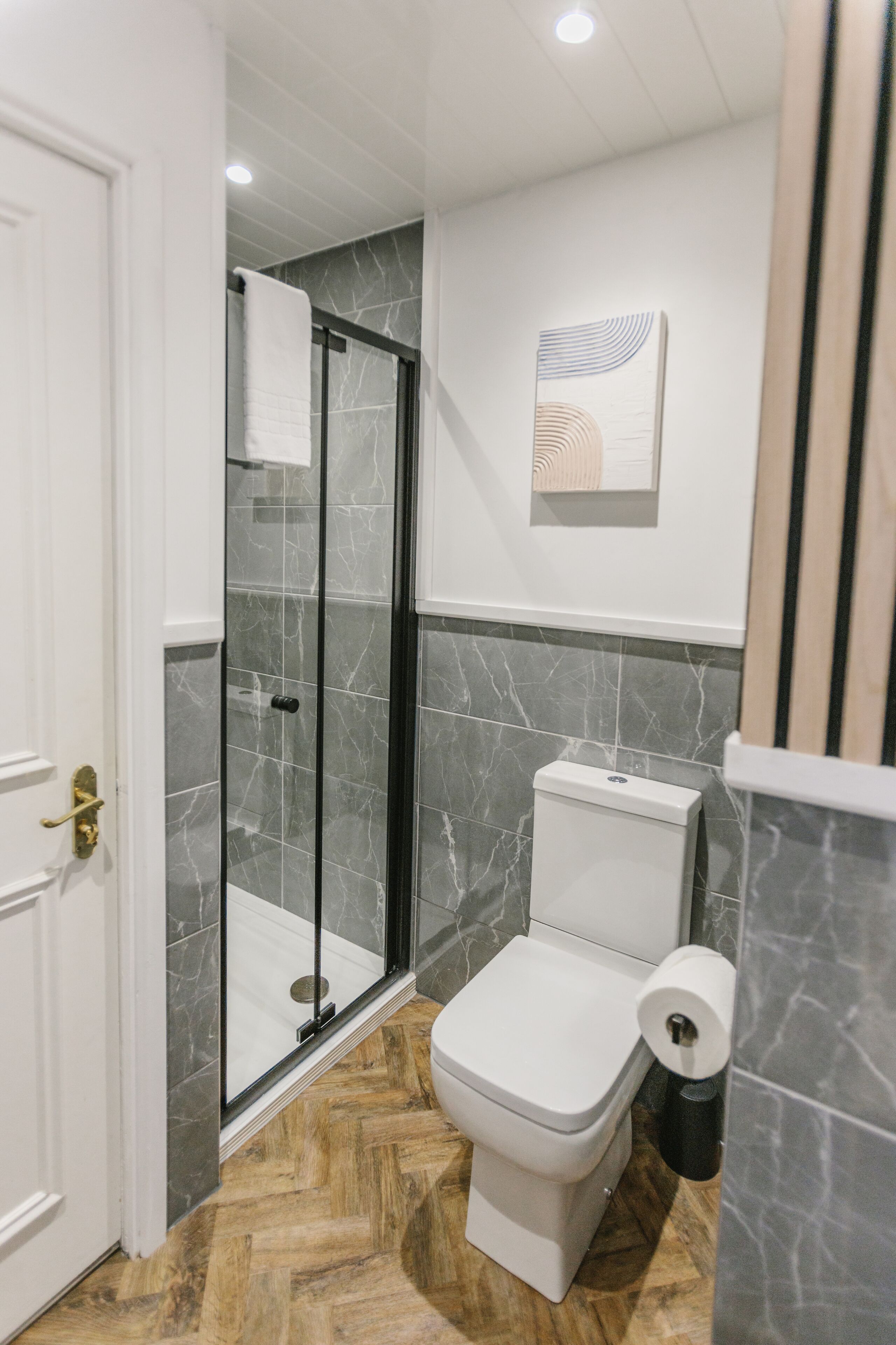 A modern bathroom with a glass-enclosed shower, a toilet, and a marble-tiled floor.