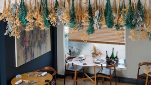 A dining area with wooden tables and chairs, a large abstract painting on the wall, and a window with blinds. - Haar with Rooms (St. Andrews)