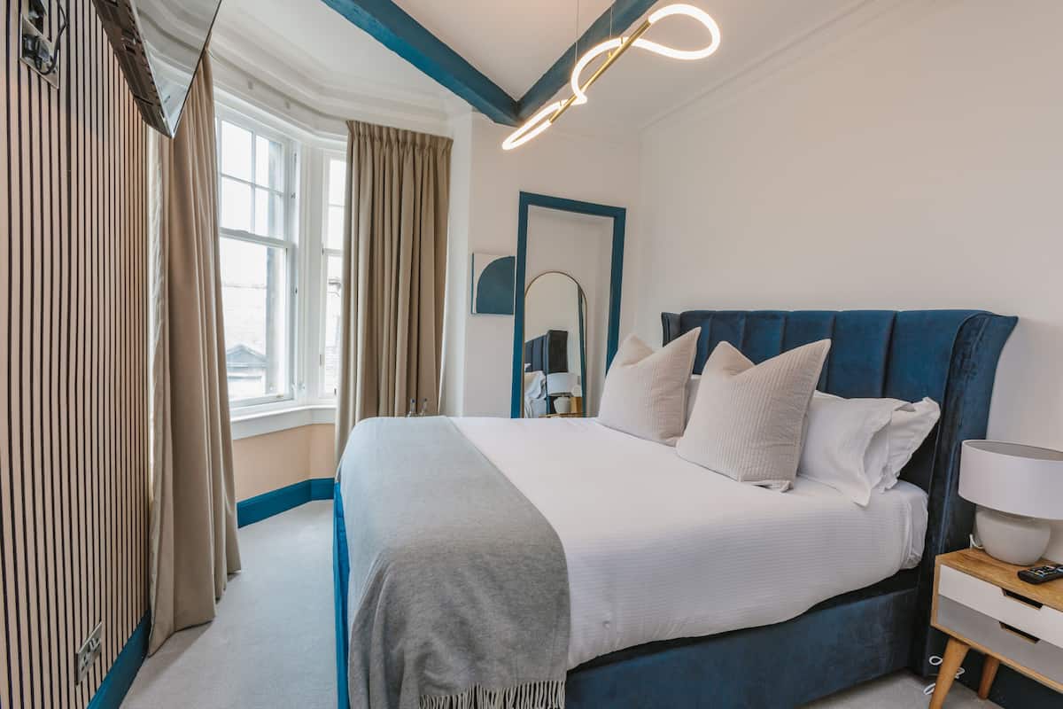A modern hotel room with a large bed, a bedside table with a lamp, and a view of the city through the window.
