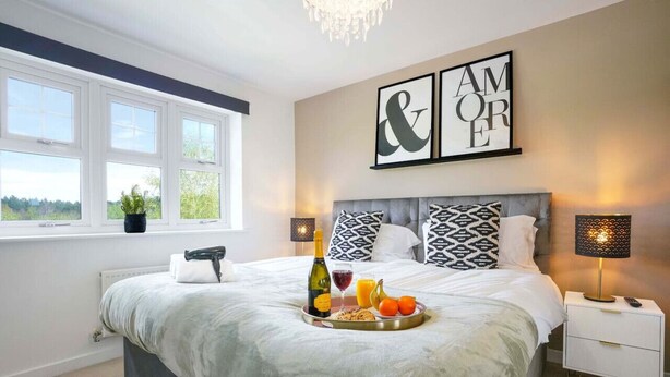 A bedroom with a large bed, bedside lamps, a tray with breakfast, and a view of greenery outside. - Detached House • Free Parking • FastWifi • SmartTV (Northampton)