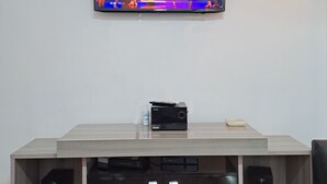 Un téléviseur à écran plat fixé au mur, un meuble de rangement en bois en dessous, équipé d’un chargeur Samsung de 800 W, et deux haut-parleurs.