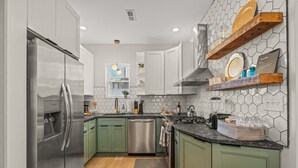 A modern kitchen with green cabinets, stainless steel appliances, and a hexagonal tile backsplash. - Clean and Comfy | King Bed | Steps to Fishtown Fun (Philadelphia)
