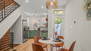 A modern kitchen with white cabinets, a stainless steel refrigerator, and a dining area with a round table and four chairs. - Clean and Comfy | King Bed | Steps to Fishtown Fun (Philadelphia)