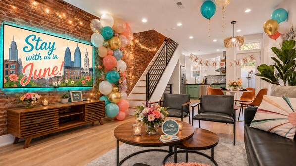 Una sala de estar con televisión mostrando un paisaje urbano, una escalera y un letrero que dice 'hello June'.