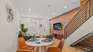 A dining area with a round table, orange chairs, and a brick wall. - Clean and Comfy | King Bed | Steps to Fishtown Fun (Philadelphia)
