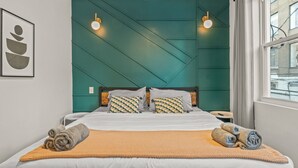 A neatly made bed with a patterned pillow, a rolled towel, and a textured blanket. - Clean and Comfy | King Bed | Steps to Fishtown Fun (Philadelphia)