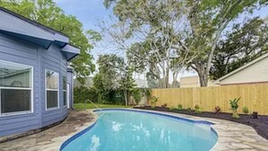Una piscina con baldosas de piedra, rodeada por una valla de madera y árboles.