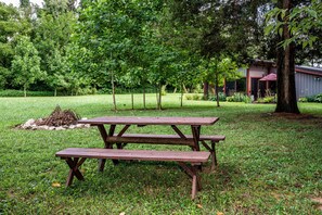 Een picknicktafel in een grasrijke omgeving met bomen en een gebouw op de achtergrond.