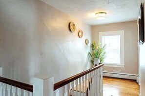Una escalera con barandilla de madera y balaustradas blancas, una pared con tres piezas decorativas circulares, una planta en maceta y una ventana con persianas.
