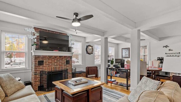A living room with a fireplace, a ceiling fan, a bookshelf, and a coffee bar. - Charming & Historic 2BR Oasis in Downtown Luxury (Manchester)