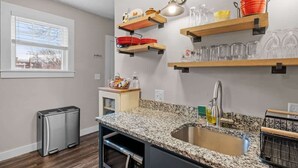 A kitchen with granite countertops, a stainless steel sink, and wooden shelves above holding dishes and glasses. - Charming & Historic 2BR Oasis in Downtown Luxury (Manchester)