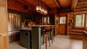 A rustic kitchen with wooden walls, a stainless steel refrigerator, a wooden island with stools, and pendant lighting.
