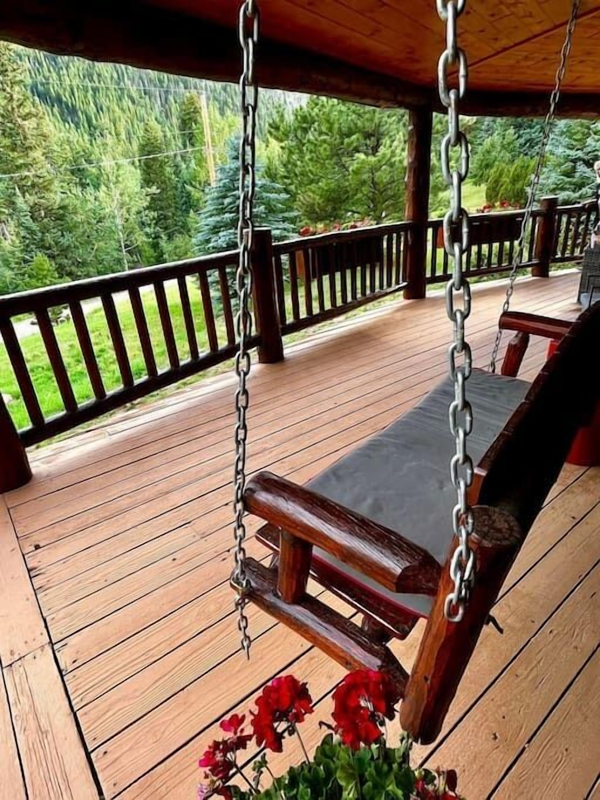 Une terrasse en bois avec une chaise suspendue et une rambarde.