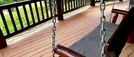 Une terrasse en bois avec une chaise suspendue et une rambarde.