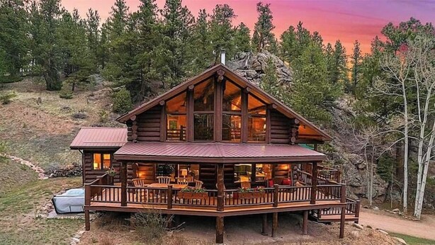 A log cabin with a large deck, multiple windows, and a stone fireplace.