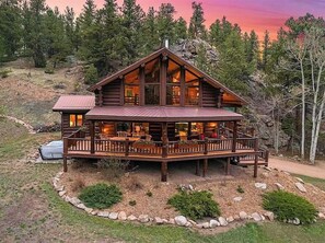 A log cabin with a large deck, multiple windows, and a stone fireplace.