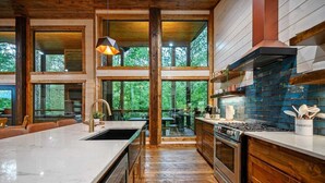 A modern kitchen with a large island, wooden cabinets, and a view of the outdoors. - Cozy Nights Cabin Luxury and Location (Broken Bow)