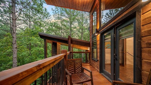 A wooden deck with a glass door leading to a room, surrounded by forest. - Cozy Nights Cabin Luxury and Location (Broken Bow)