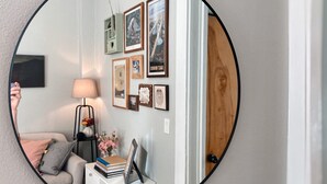 A round mirror reflecting a living room with a sofa, a lamp, a side table with books and flowers, and a wall with framed pictures. - Charming River View Apt | Walk to Shops & Cafes (The Dalles)