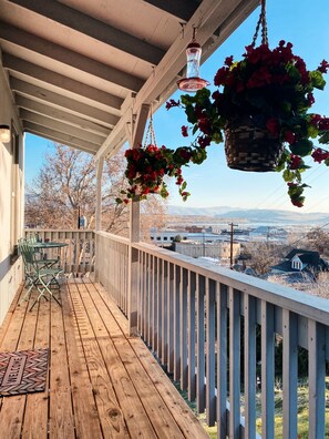 Eine Holzdar Terrasse mit Geländer, Fußmatte und hängenden Blumenkörben.