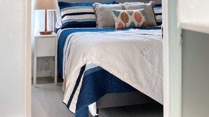 A bedroom with a bed, a bedside table with a lamp, a window, and a hanging light fixture. - Charming River View Apt | Walk to Shops & Cafes (The Dalles)