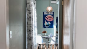 A hallway with a dining area featuring a table and chairs, a hanging light fixture, and a wall poster. - Charming River View Apt | Walk to Shops & Cafes (The Dalles)