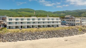 A multi-story hotel with balconies, located near a rocky shoreline with a backdrop of green hills. - Rockaway Beach Resort (Rockaway Beach)