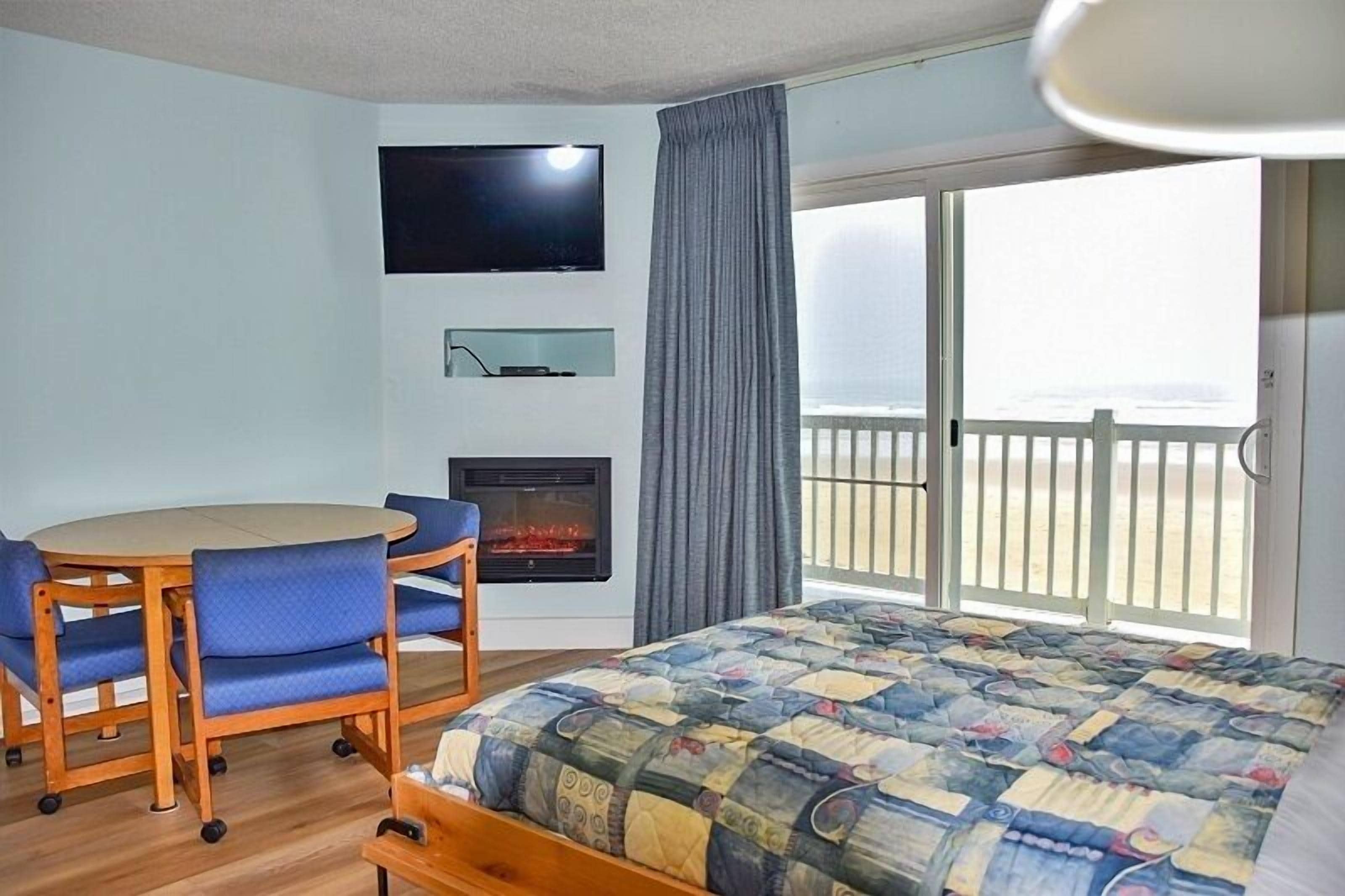 A hotel room with a bed, a TV, a fireplace, a balcony with a railing, and a view of the sea.