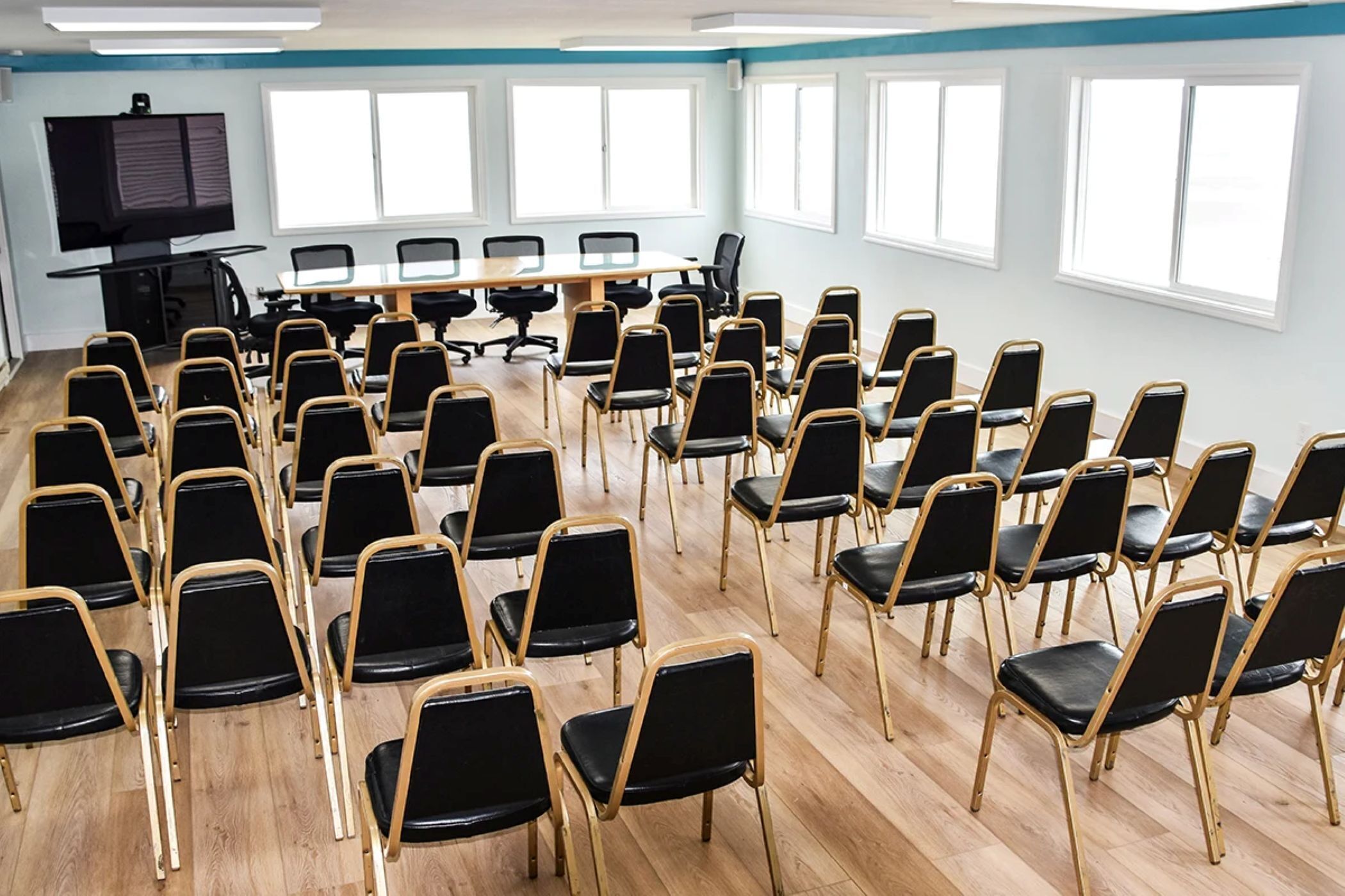A conference room with rows of black chairs, a long table, and large windows.