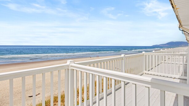 A beach view from a wooden deck with a railing, overlooking the ocean and sandy beach. - Rockaway Beach Resort (Rockaway Beach)