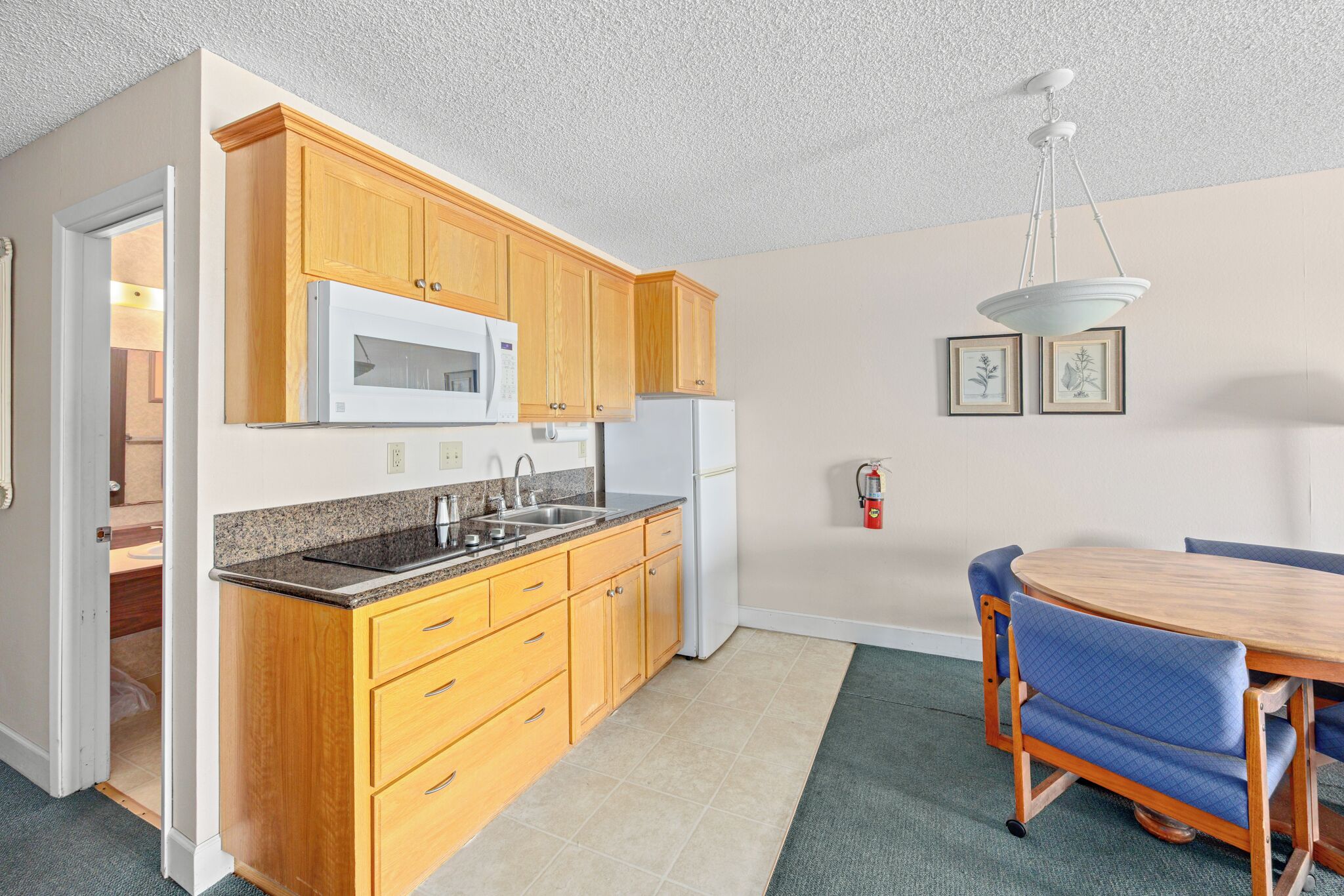 A kitchen with wooden cabinets, a microwave, a refrigerator, a sink, and a dining table with chairs.
