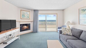 A living room with a television, fireplace, sofa, and a balcony with a view of the sea. - Rockaway Beach Resort (Rockaway Beach)