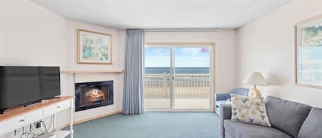A living room with a television, fireplace, sofa, and a balcony with a view of the sea.