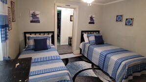 Quarto com duas camas, um ventilador de teto e uma porta que dá para outro cômodo.