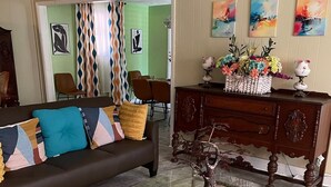 Uma sala de estar com um sofá marrom, almofadas coloridas, uma mesa de centro de vidro, um armário de madeira e um tapete estampado.