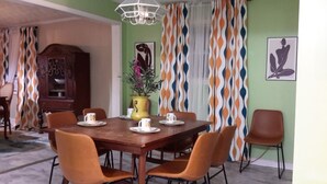 Uma área de jantar com mesa de madeira, cadeiras laranja e um vaso amarelo com flores.
