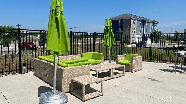 An outdoor patio area with wicker furniture, green cushions, and a metal table.