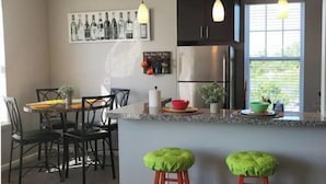 A modern kitchen with a central island, pendant lights, and a dining area with chairs and a table.