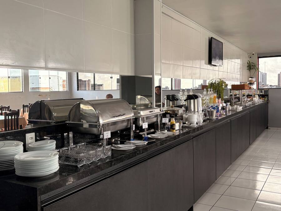 Una cocina moderna de hotel con barra de buffet, que incluye una estación de autoservicio, una máquina de café y un amplio ventanal con vistas a la ciudad.