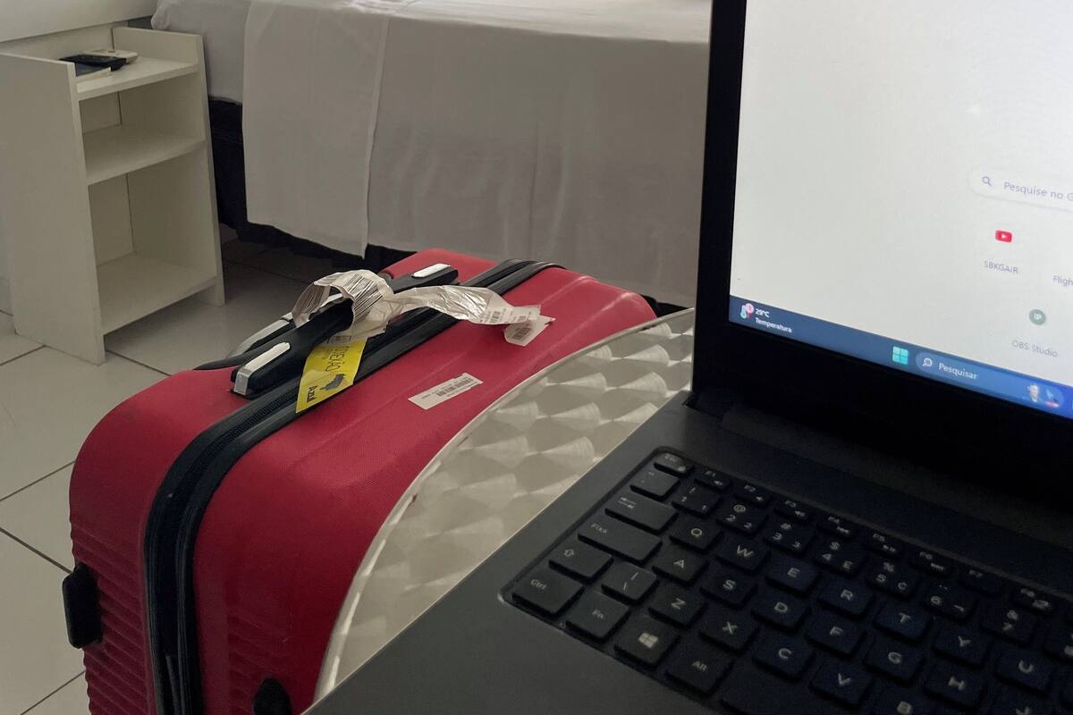 A hotel room with a bed, a laptop on a desk, and a suitcase.
