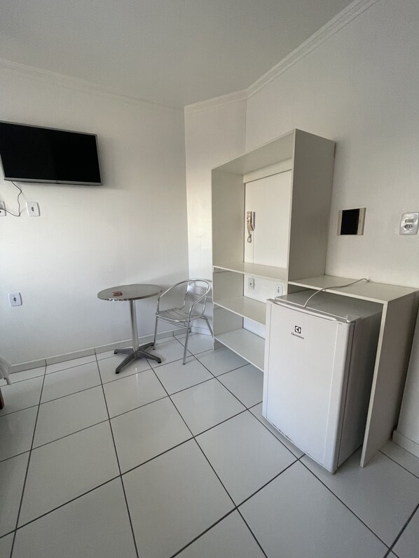 A small, clean room with a tiled floor, a desk with a chair, a flat-screen TV mounted on the wall, and a compact refrigerator. - Hotel Pousada Acauã (Campina Grande)