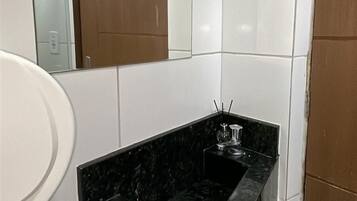 Une salle de bain avec des carreaux blancs, un lavabo en marbre noir et un miroir.