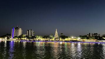 Un paisaje urbano nocturno con edificios iluminados, un río que refleja luces y un árbol de Navidad destacado.
