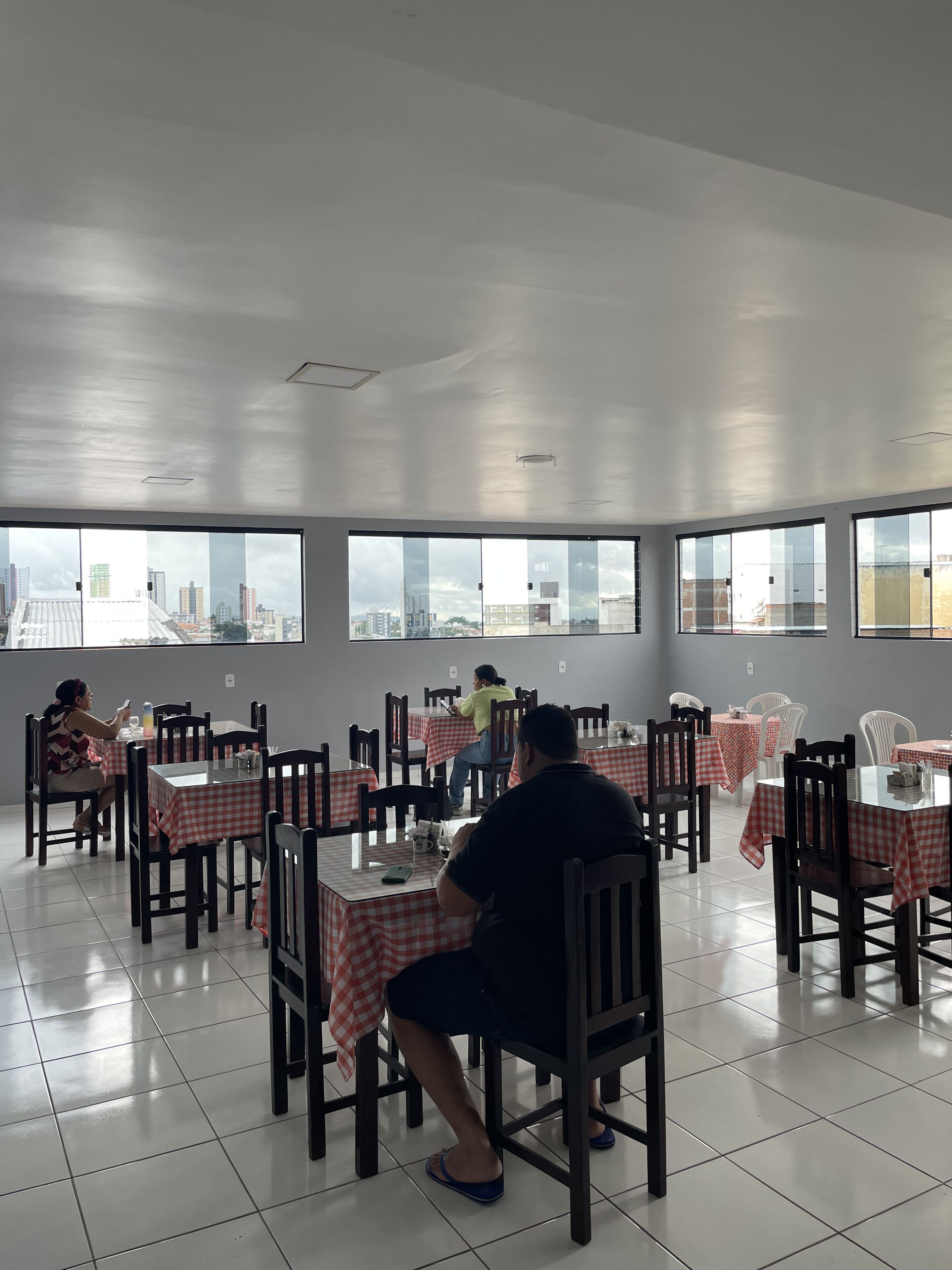 A dining area with checkered tablecloths, wooden chairs, and large windows offering city views.