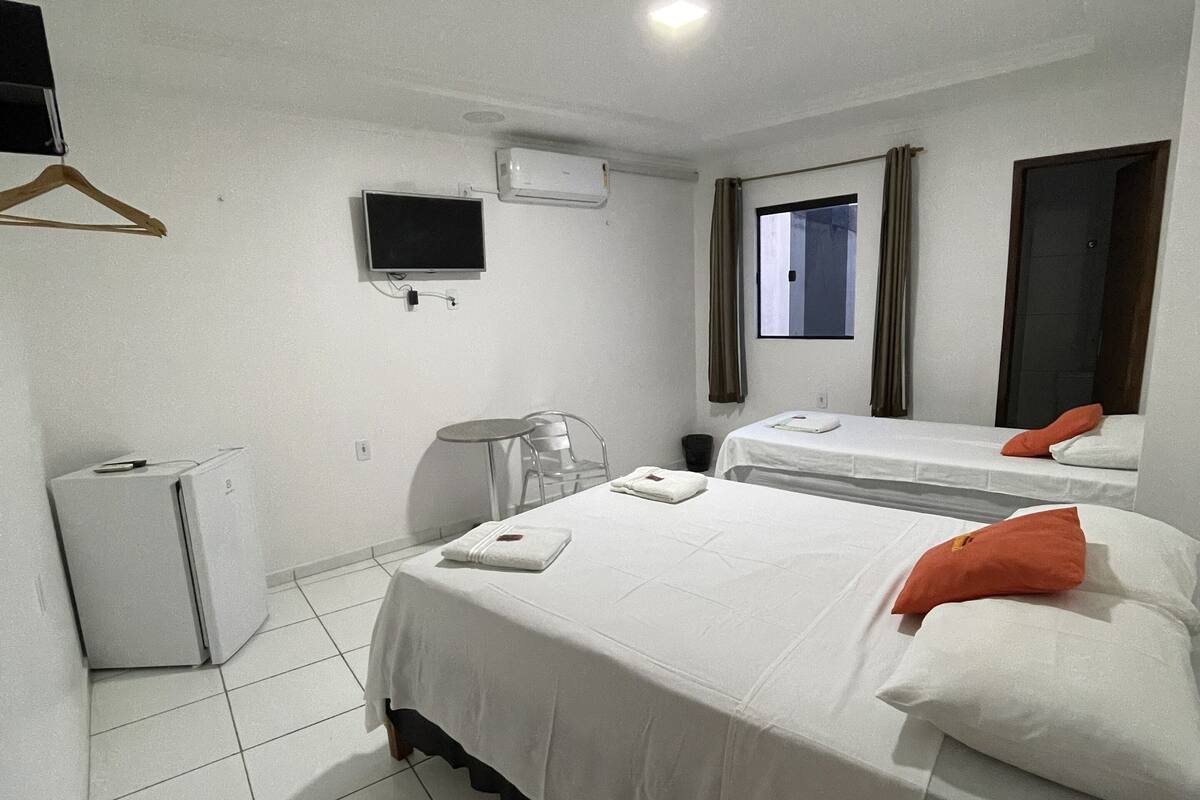 A hotel room with a bed, a desk, a chair, a TV, and an air conditioner.