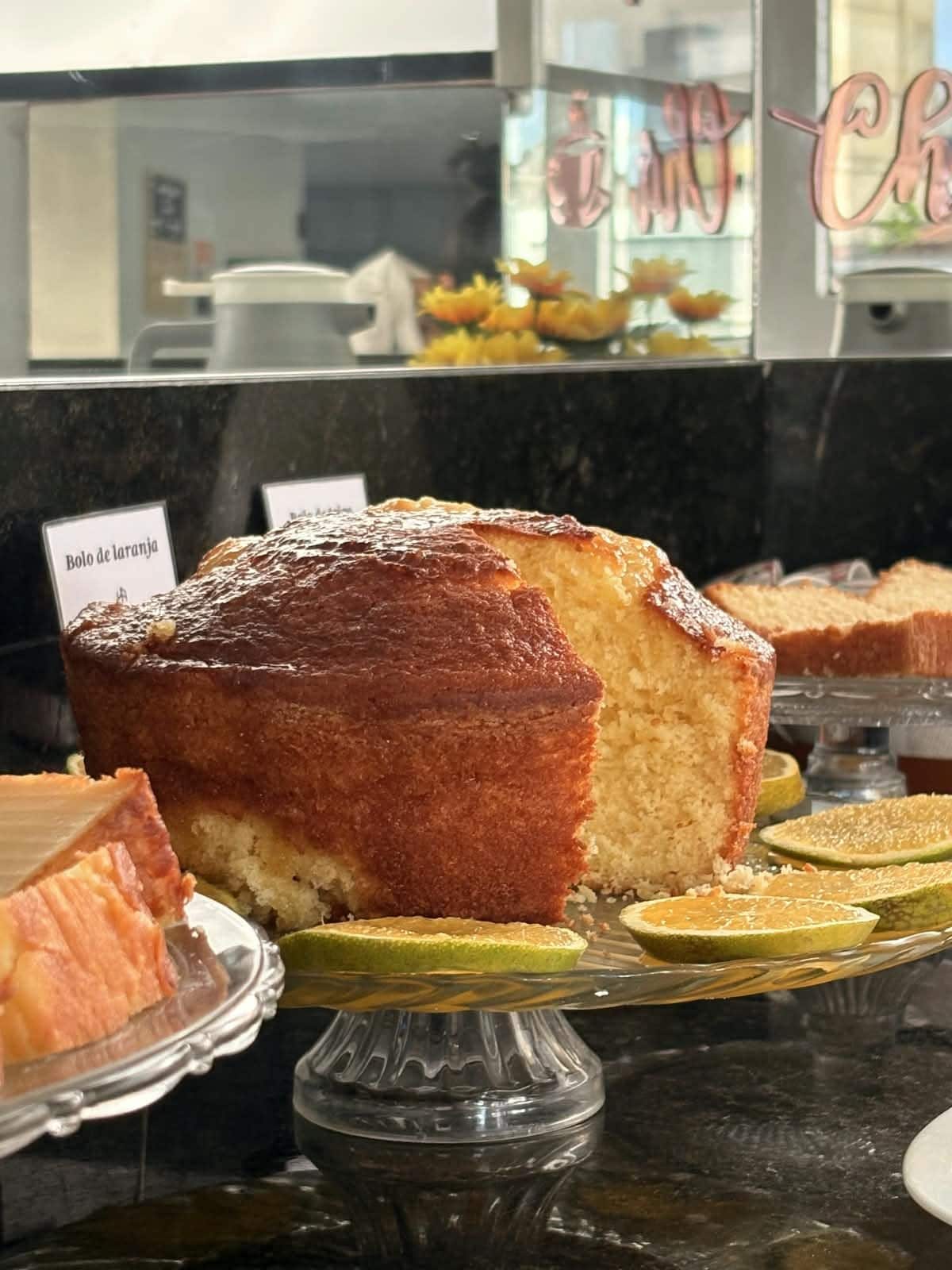 Une présentation de desserts comprenant un gâteau étiqueté « Bolo de Laranja » et des tranches de citron vert.