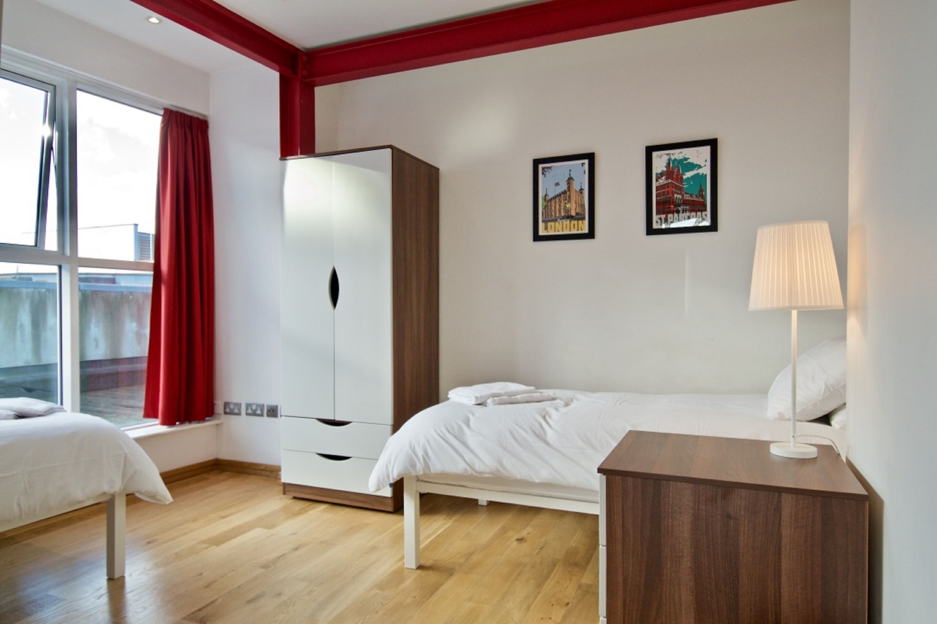 A bedroom with a bed, a wardrobe, a bedside table, and a window with curtains.