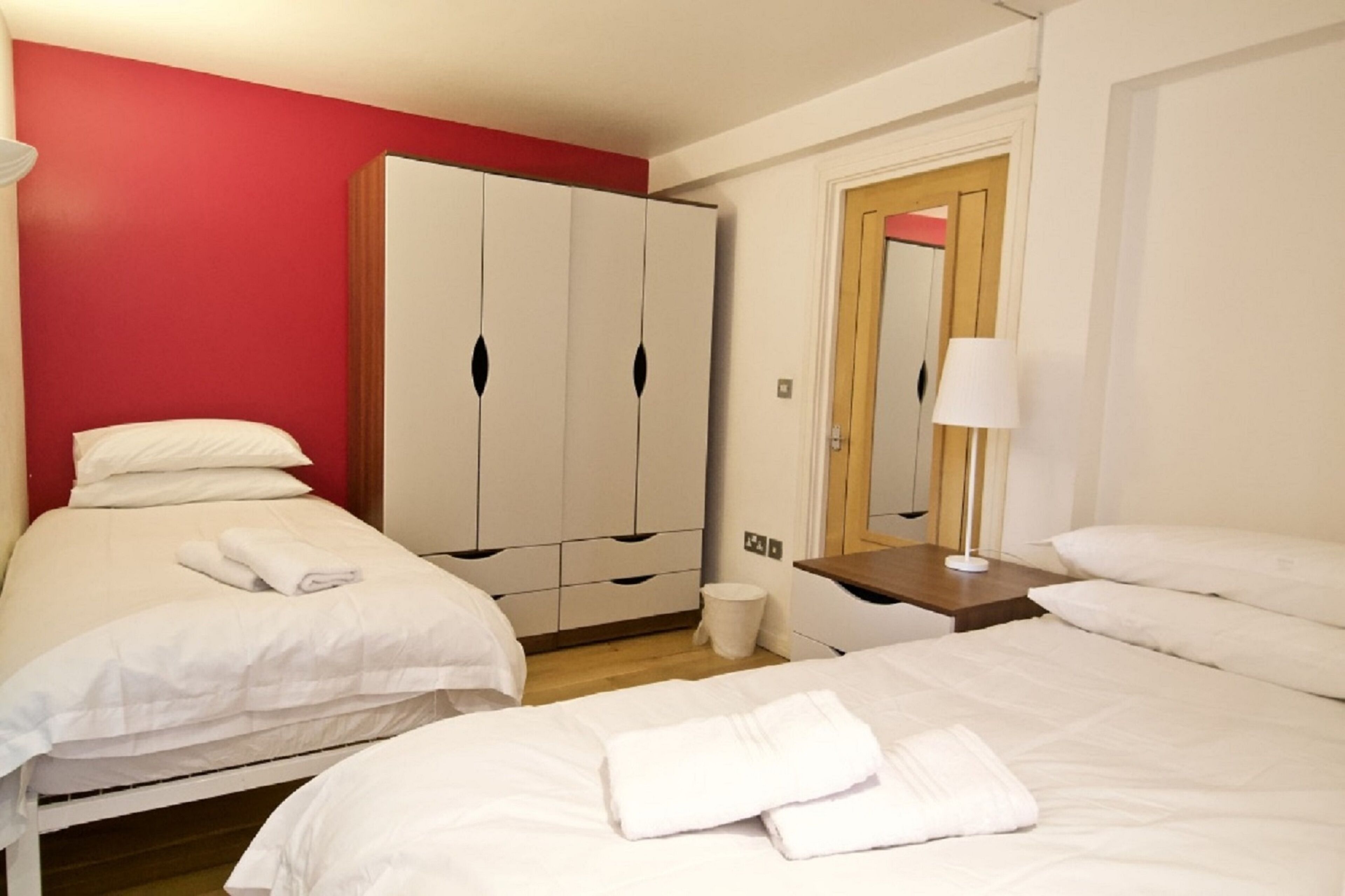 Habitación de hotel con dos camas, un armario, un espejo y una mesita de noche.