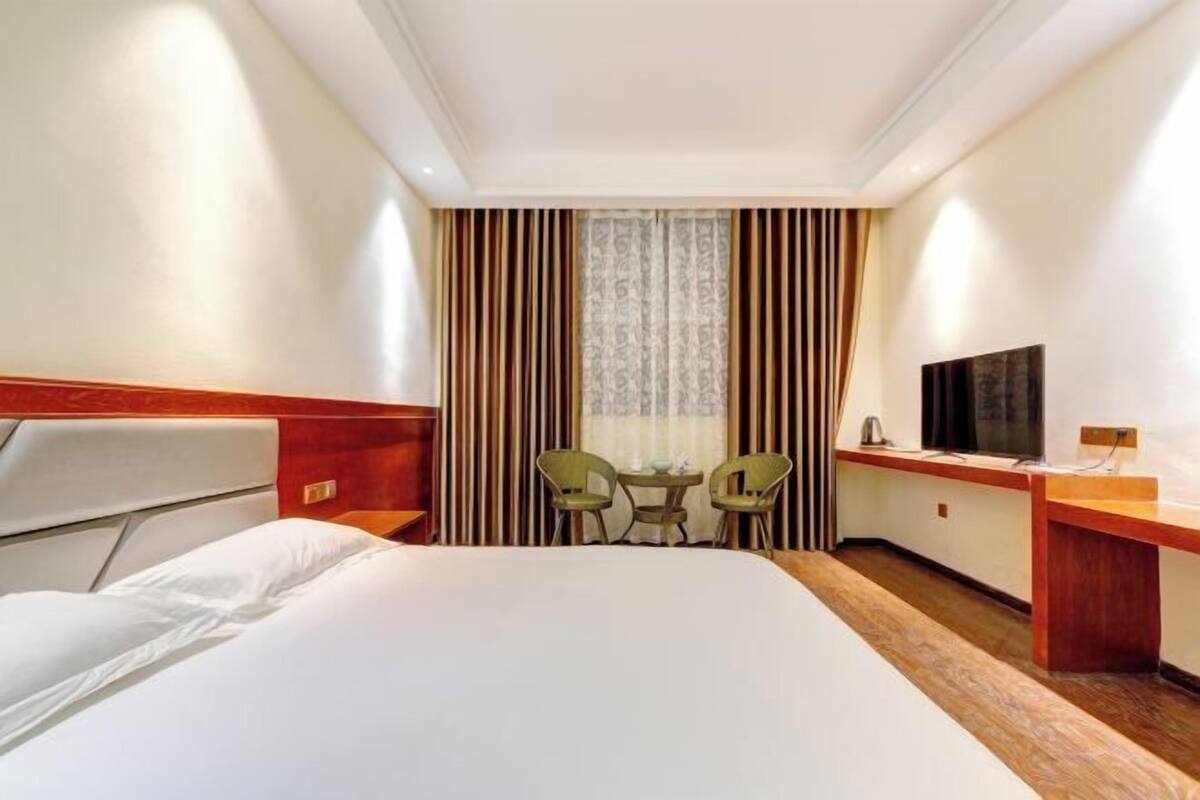 A hotel room with a large bed, a desk with a television, two chairs, and a window with curtains.